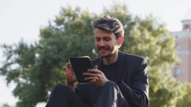 Bahçede tablet karıştıran genç bir adam. Düşünceli işadamı şifreli paraya çok para yatırmaya karar verdi. Dışarıdaki haberleri araştırmak için mini bilgisayar kullanan bir adam. Dinlendirici öğrenci kitabı. Yüksek kalite