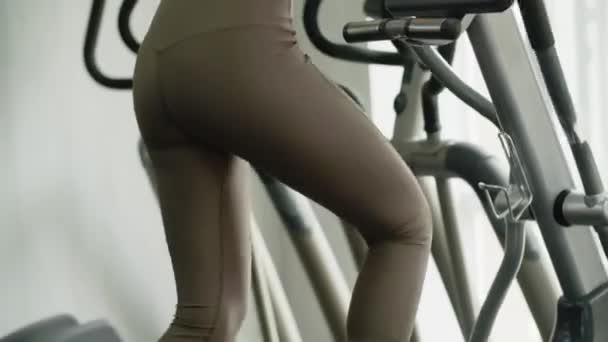 一个身材苗条的年轻女运动员在体育馆里骑着一部健身机 容易而且相当有规律的训练 对身体有益 在一次行动中令人愉快地放松 女人看着窗户 — 图库视频影像
