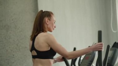 Genç, narin, atletik bir kız spor salonunda hızlı bir egzersiz makinesi kullanıyor. Hızlandırılmış eğitim rejimi. Bir kadın, spor formunun istenen sonucunu güvenle elde etmeye çalışır. Hazırlanıyor...
