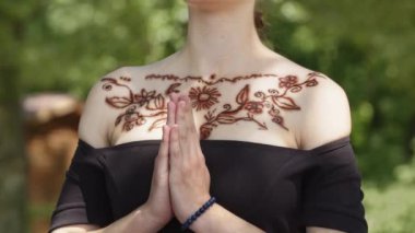 Göğsünde kızılderili desenli kına dövmesi olan siyah elbiseli bir kız. Doğu bayramında veya festivalde bulunan genç bir kadın meditasyon yapar, dua eder ve avuçlarını göğsüne yaklaştırır. Barış jesti ve