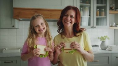 Kızları olan pozitif anne mutfakta sandviçlerle durup birbirlerine şefkat gösteriyorlar. Anne ve çocuk gülümseyerek poz veriyor ve kameraya bakıyor. Konsept: