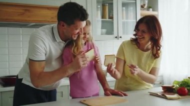 Mutfakta gülümseyen bir Amerikan rüya ailesi eğlenceli sandviçler yapıyor. Kız, anne ve babasının piknik ya da misafirler için atıştırmalık hazırlamasına yardım ediyor. Sağlıklı beslenme gösterisi. Yüksek