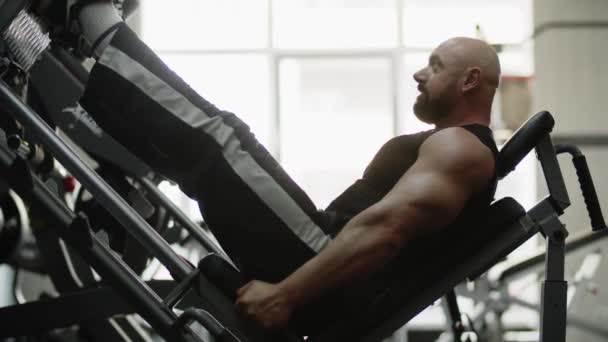 男子健美健美运动员在健身房的训练集中在机器上 锻炼腿的力量和耐力 运动员上下弯曲和伸展他的腿 高质量的4K镜头 — 图库视频影像
