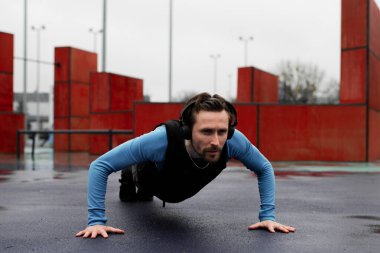 Şınav çeken güçlü genç bir atlet. İki elini de yere koy sporcu. Çaba meyvesini veriyor. Yetişkin bir adam oyun alanında tek başına egzersiz yapıyor. Yatay çizgi. Yağmurlu hava egzersizi. Yüksek