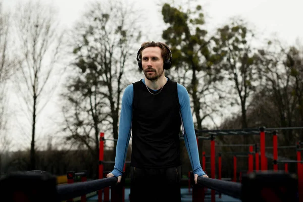 Sabah eğitimi kavramı. Sağlıklı bir yaşam tarzı. Sporcu metal saplar üzerinde denge egzersizi yapıyor. Sportif yetişkin adam paralel barlar kullanarak şınav çekiyor. Jimnastik için yatay ekipman. Yoğunlaşmış