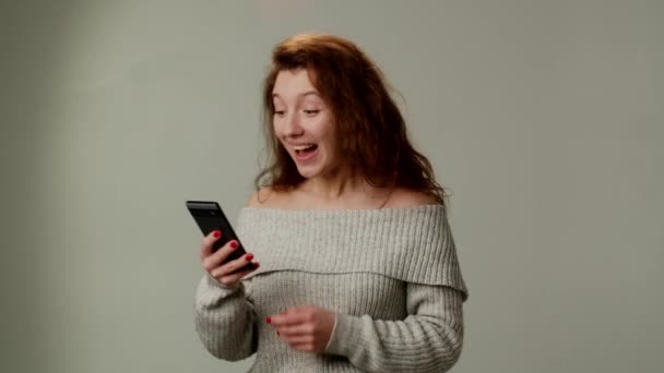 Μια Θετική Νεαρή Κοπέλα Χρησιμοποιεί Ένα Smartphone Και Χαρούμενος Έντονα — Αρχείο Βίντεο