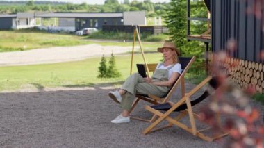 Orta yaşlı bir kadın yaz tatilini kır evinde geçirir, açık havadan ve işten sonra bahçede dinlenerek, sakin bir ortamda bir koltukta oturur. Bir bayan okumak için tablet kullanıyor.