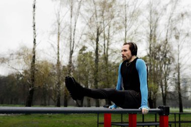 Parkta karın kasları olan bir sporcu. Profesyonel sporcu vücudunu maratona hazırlıyor. Erkek jimnastikçi, karın kaslarını paralel parmaklıklar kullanarak çalıştırıyor. Yüksek kalite fotoğraf