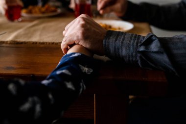 Yemek masasında ailenin el ele tutuşmasını yakından çek. Hıristiyanlar yemekten önce dua eder. Ruhsal gelenek, kollarını masanın üstüne koymak. Katolik kilisesine inananlar aileleri Tanrı 'ya şükrediyor. Yüksek