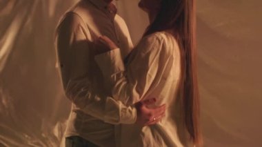 Stüdyodaki sarılan çiftin arka plandaki ışıkları kapatma hareketi. Genç erkek arkadaş, kız arkadaşıyla evde sarmaş dolaş. Yıldönümü çekimleri için beyaz kıyafetler giyen romantik bir çift. Yüksek