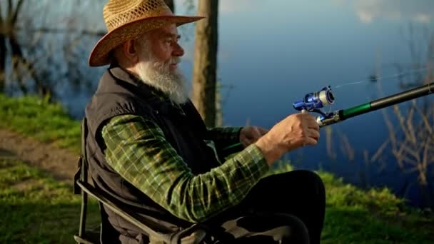 最喜欢的业余爱好的概念 在河边钓鱼时 放松坐在椅子上的养老金领取者 满意的祖父在户外处理纺鱼棒 退休的垂钓者 高质量的4K镜头 — 图库视频影像