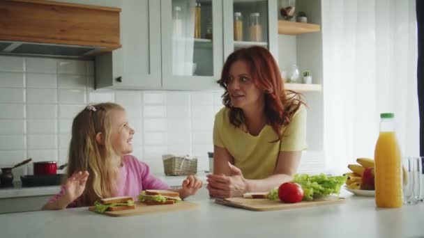 笑顔の母親と娘が台所のテーブルに立って 遊び心のある方法で料理のレシピについて話し合っている 幾何学的なサンドイッチの形のための創造的な考えの仮想スケッチを共有して下さい イギリス — ストック動画