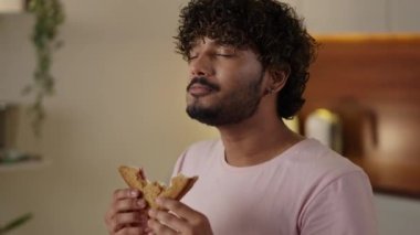 Aldatma yemeği kavramı. Genç Hintli adam büyük sandviç yiyor ve kahve içiyor. Günaydın geleneksel kahvaltı. Mutfakta lezzetli tost yiyen adam. Erkek öğrenci öğle yemeğinin tadını çıkarıyor. Yüksek kalite 4k