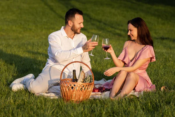 Shot of beautiful couple in park picnic outdoors. Loving married family drinking red wine sitting on blanket. Romantic date outside. Happy family enjoy drinks grapevine at nature. High quality photo