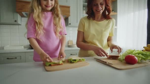 キッチンで娘とフレンドリーで笑顔の母親は サンドイッチを折り畳んで暖かく抱き合っています 良い仕事のための5つのジェスチャーを示しています 幸せな母性と子供時代の概念 — ストック動画