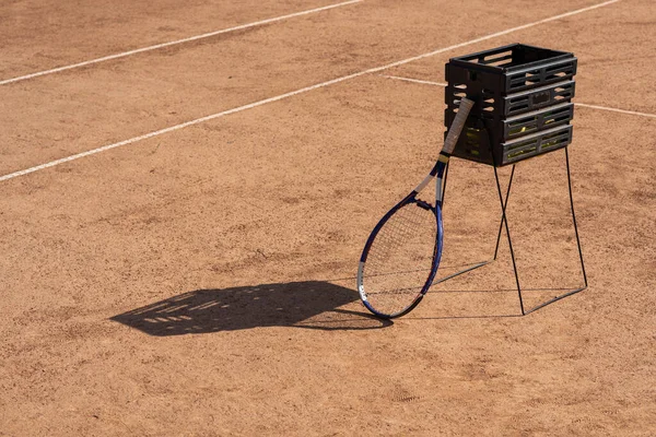 Ball machine for tennis. Professional robot for training experienced tennis players standing on court. Box prepared to take tennis balls. Racket leans on the ball basket. High quality photo