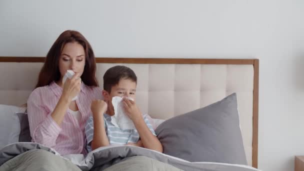 生病的母亲和儿子躺在卧室的沙发上 把鼻涕抹到一次性餐巾纸上 挥动着鼻涕 母亲和孩子感染了流感或感冒 在家里接受治疗 — 图库视频影像