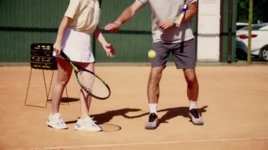 Bir kız tenisçi topa vurmak için antrenman yapıyor. Tenis koçu gözlemler ve koğuşuna raketi doğru tutması gerektiğini gösterir. Genç bir bayan sporcu antrenör gözetiminde hazırlanıyor.