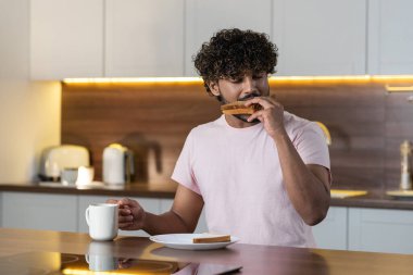 Huysuz bir adam mutfakta durmuş, elinde bir kupa tutuyor, sandviç yiyor ve zevkle çay ya da kahve içiyor. Genç bir Amerikalı ya da Afrikalı adam atıştırmalıktan hoşlanır.