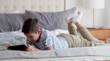 Küçük bir çocuk karnının üstüne yatar ve ayaklarını yatak odasındaki kanepeye koyar. Bir çocuk komik bir film ya da çizgi film izler, tablet kullanır, gülümser ve güler. Mutluluk kavramı ve