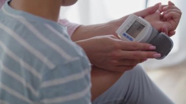 Yatak odasında kolunda dijital tonometre olan küçük bir çocuk. Bir anne, oğlunun nabzını ve kan basıncını ölçer ve sağlık göstergelerini kontrol eder. İlgili bir anne çocuğunu okşar ve geçindirir.