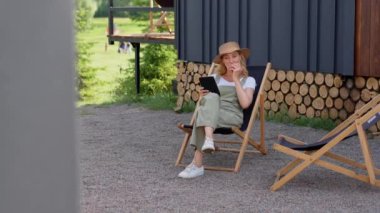 Orta yaşlı bir kadın yaz tatilini kır evinde geçirir, açık havada eğlenir, işten sonra bahçede dinlenir, elma yer, bir koltukta oturur. Bir bayan okumak ve izlemek için tablet kullanır.