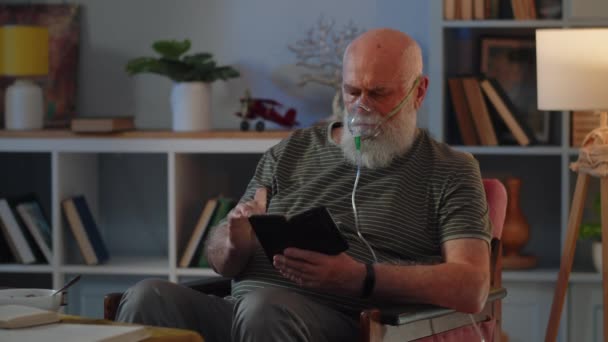 Alter Mann Mit Atemmaske Bleibt Auf Stuhl Sitzen Und Liest — Stockvideo