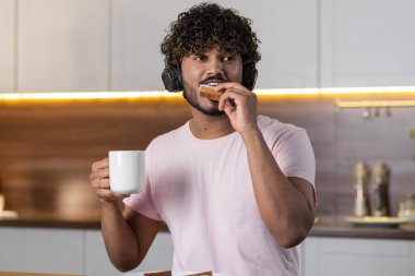 Olumlu bir mestizo adam mutfakta duruyor, elinde bir fincan çay ya da kahve tutuyor, sandviç yiyor, kulaklıkla zevkle müzik dinliyor ve uzaktan bakıyor. Amerikalı ya da Afrikalı