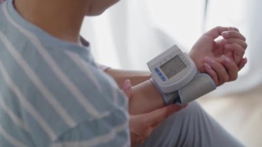 Yatak odasında kolunda dijital tonometre olan küçük bir çocuk. Bir anne, oğlunun nabzını ve kan basıncını ölçer ve sağlık göstergelerini kontrol eder. Bir anne çocuğunu okşar ve ona destek olur.