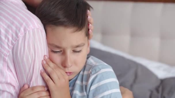一个年轻的母亲和一个悲伤的小男孩一起坐在床上 表现出温暖的关怀和感情 一位有爱心的母亲轻抚 拥抱她那悲伤 烦躁的儿子 — 图库视频影像