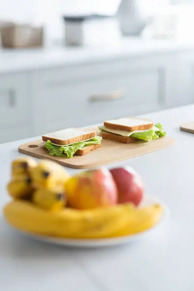 キャベツとチーズが付いている準備ができたサンドイッチは台所の木製板にあります 前景にリンゴとバナナが付いている皿 ブラー効果 クローズアップ 選択的なフォーカスモード 高品質の写真 — ストック写真