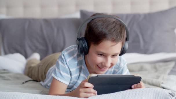 Malý Chlapec Leží Břiše Pohovce Ložnici Používá Tablet Sluchátka Dítě — Stock video