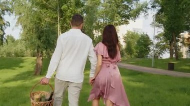Park 'ta piknik yapmak için el ele tutuşurken aile fotoğrafı. Sevgilisi olan erkek arkadaşı dışarıda yıldönümü kutlaması için bir yer seçmiş. Piknik sepeti. Yüksek kalite 4k