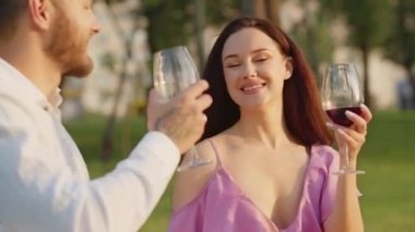 Yaz pikniğinde şarap içen sevgi dolu bir çift. Mutlu genç aşıklar açık havada kırmızı üzüm suyu içerken romantik atmosferin tadını çıkarıyorlar. Şenlik kıyafetleri içinde iki sevimli insan park geçmişine tezahürat yapıyor.