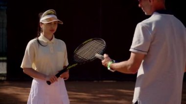 Bir erkek antrenör ve kız koğuşu, ortak antrenman sonrasında spor sahasında duruyor ve maçı yönetmedeki eksiklikler ve gelişmeler hakkında fikir alışverişinde bulunuyor. Tenis antrenörü tavsiyelerde bulunur.