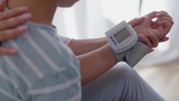 ベッドルームの小さな少年が腕にデジタルテノメーターを装着した 母親は 健康指標を監視しチェックするために息子の脈拍と血圧を測定します 母親は彼女の子供を背負って彼をサポート — ストック動画