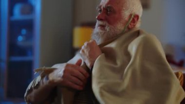 Yaşlı bir adam bakım evinde ya da bronşiyal astımı olan bir hastanede solunumu kolaylaştırmak için oksijen maskesi kullanır. Hasta bir insan odada oturur, üşüdüğünü hisseder ve ekoseyi omuzlarında tutar.
