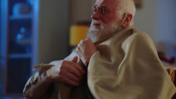 一位老年男子在疗养院或医院里 患有支气管哮喘 他使用氧气面罩来缓解呼吸 一个病人坐在房间里 感到冷 调整肩膀上的格子花以保持身体的健康 — 图库视频影像