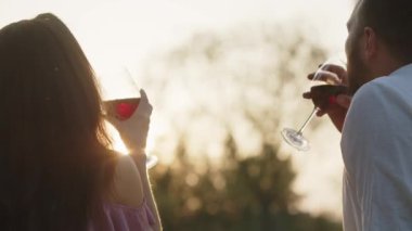 Kırmızı şarap kadehli çift bahçede piknikte gün batımını izliyor. Kafkasyalı mutlu bir aile şarap içip açık havada güneşe bakıyor. Romantik randevu kavramı. Yüksek kalite 4k görüntü