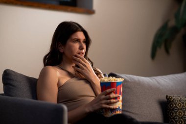 Patlamış mısırlı endişeli genç kadın televizyon izliyor. Kız film izlerken şaşkınlığını dile getiriyor. Yüksek kalite fotoğraf