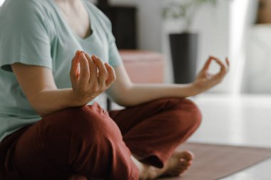 Orta yaşlı bir bayan evde yoga yapıyor. Yüzü olmayan bir kadın, nilüfer pozisyonundaki bir paspasın üzerinde yan yatar. Fiziksel egzersiz yoluyla ruhsal gelişim kavramı