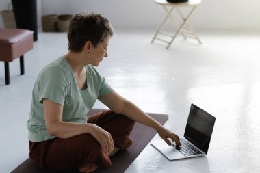 Orta yaşlı bir bayan evde yoga eğitimi aldıktan sonra dinleniyor. Ciddi bir kadın Lotus pozisyonunda yerde yan yatar, laptopunu arar ve meditasyon gevşetici müzik dinler. Üst