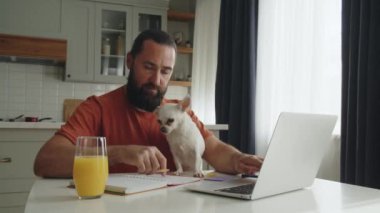 Genç sakallı bir adam mutfak masasında evcil bir arkadaşıyla birlikte oturuyor, yanında kulağını sallayan beyaz bir chihuahua köpeği, ve ilgili sahibi onu dostça okşuyor. Bir girişimci
