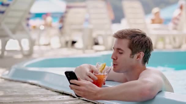 年轻人在游泳池里浏览社交媒体 喝开胃酒 商人在酒吧边消磨时光 边喝酒边发短信邀请女朋友参加聚会 泳池管理员 — 图库视频影像