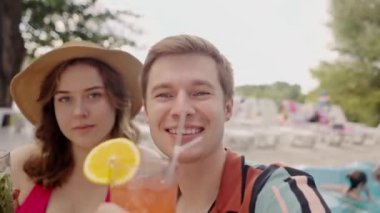 Kafkasyalı mutlu çift havuz başında birlikte eğleniyor ve kokteyl içiyor. Genç ve kız arkadaşı olan komik bir erkek arkadaş tatilde nasıl mojito içildiğini videoya kaydediyor. İki aşığın kendi portresi