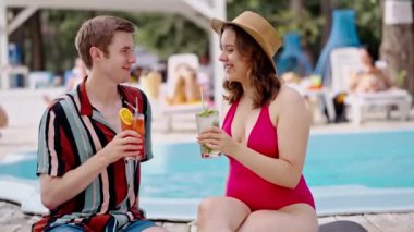 Havuz başında havuz başında taze kokteyl içen memnun insanlar. Genç erkek arkadaş ve kız arkadaş güneşlenmek için güneşleniyorlar mohito içiyorlar, su kenarında aperol içiyorlar. Açık yüzme havuzu olan bir bar.