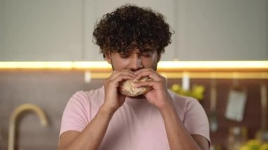 Fast food eğlencesi. Genç adam mutfakta patates kızartmasıyla sağlıksız hamburger yiyor. Yetişkin adam rahatlıyor kulaklıkları dinliyor Amerikan usulü burgeri tatmin ediyor. Aldatma yemeğini kutlayan kişi. Yüksek