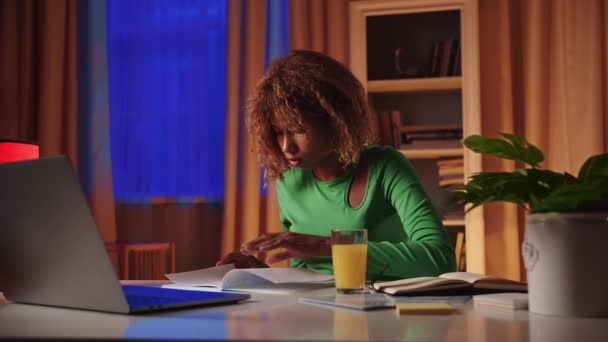 アフリカの女子生徒がテーブルに座り ノートを反転し レクチャーの情報を左手で書き留める 若い女性はラップトップとタイプを使用して教育へのリンクを検索します — ストック動画