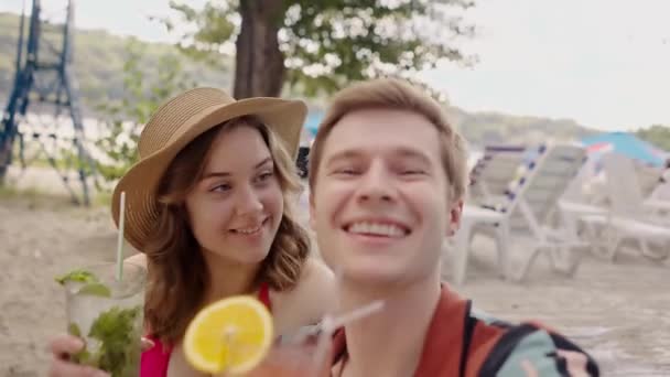 幸せな白人カップルは一緒に楽しみ プールサイドでカクテルを飲んでいます ガールフレンドとの若い面白いボーイフレンドは 休暇中に飲み物Movitoがいかにしてビデオを録画します 2人の恋人の自己肖像画 — ストック動画