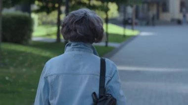 Şehirde gezen sırt çantalı emekli bir kadın kameraya doğru dönüyor. Kot gömlekli, mutlu, güzel büyükannem şehir mimarisinin mükemmelliğini görmek için geri dönüyor. Yüksek